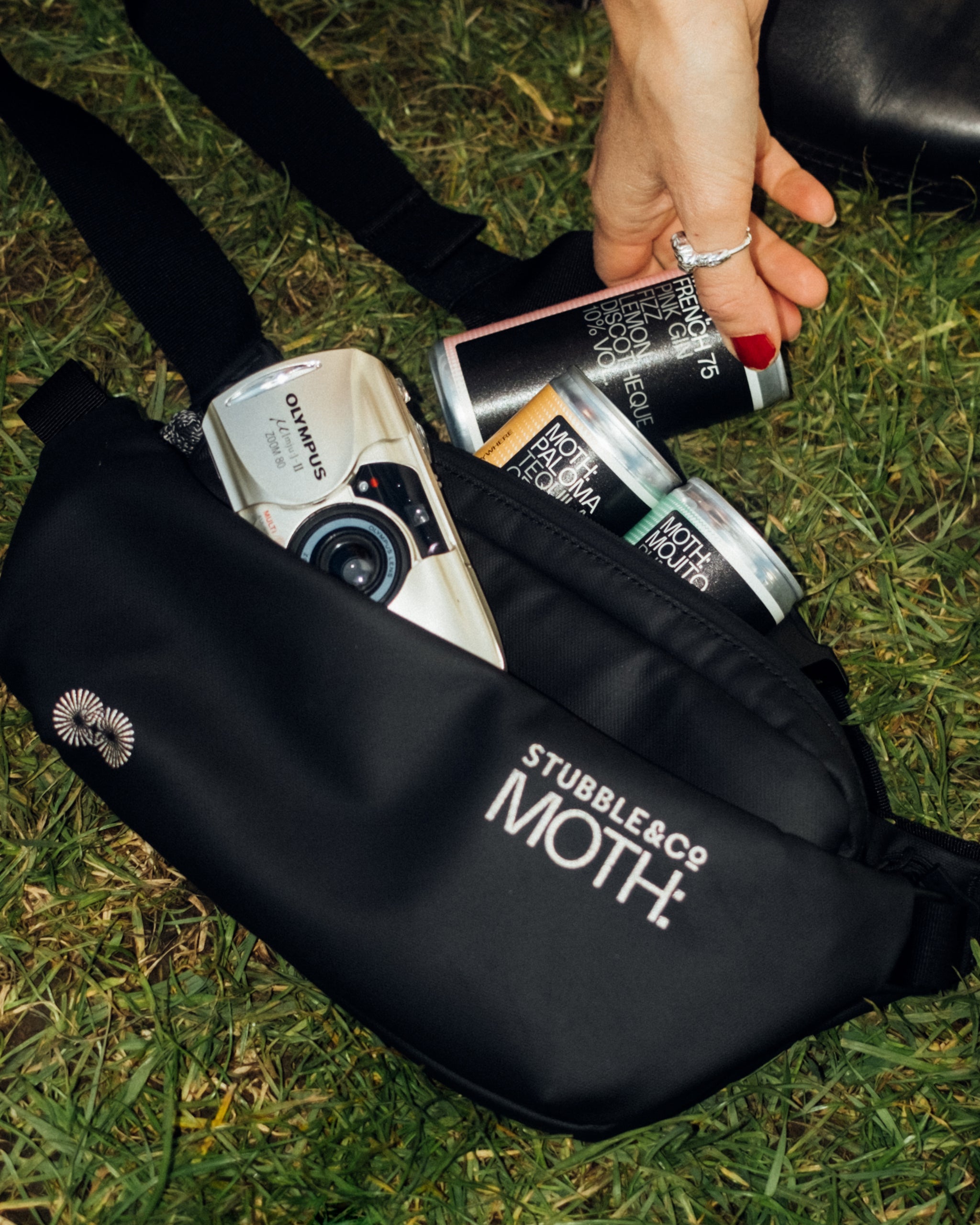 An image of the co-branded MOTH crossbody bag with cans on MOTH and a disposable camera inside.