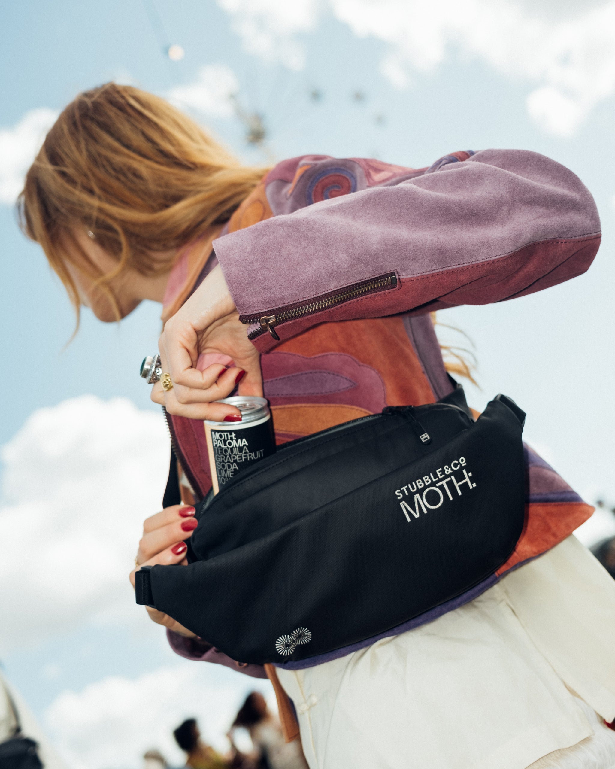 A woman wearing the co-branded MOTH crossbody bags with a MOTH drink in her hand