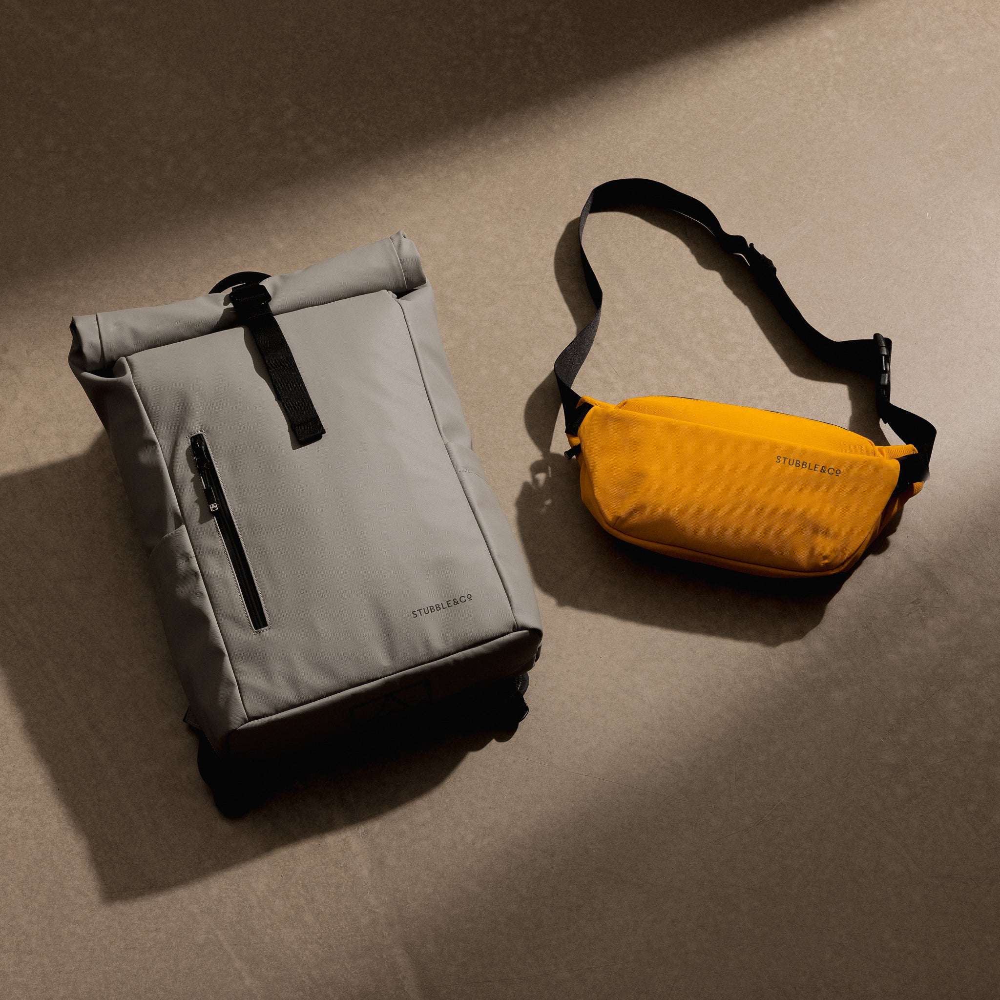 A studio shot of a roll top 15l and a yellow crossbody on the floor as a creative flat lay