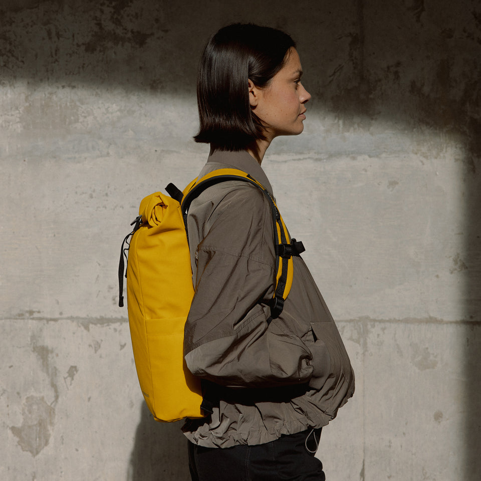 a woman wearing a Yellow roll top 15l on her back showing the side angle