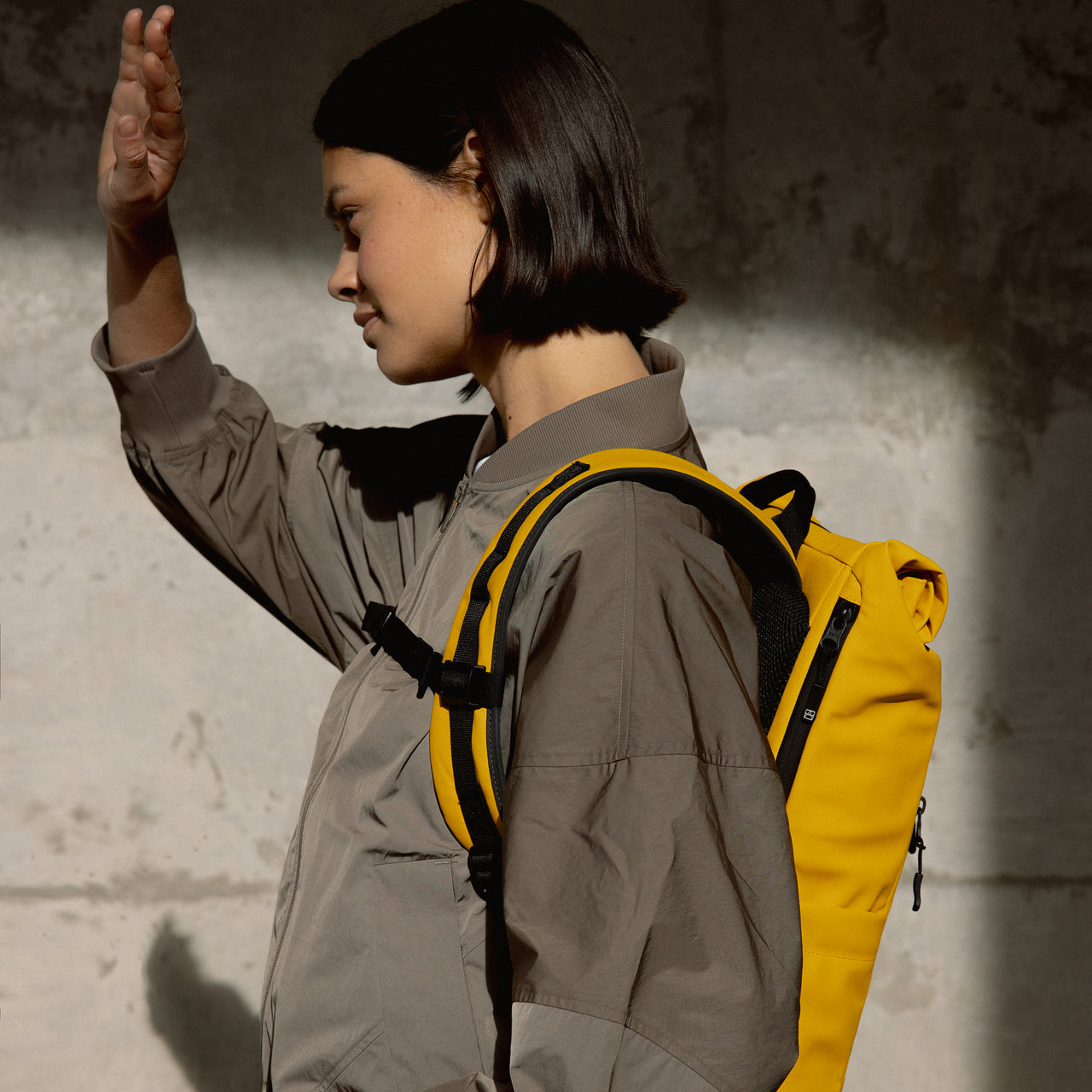 a woman standing the sunshine showing a close up of the laptop compartment on a Yellow roll top 15l