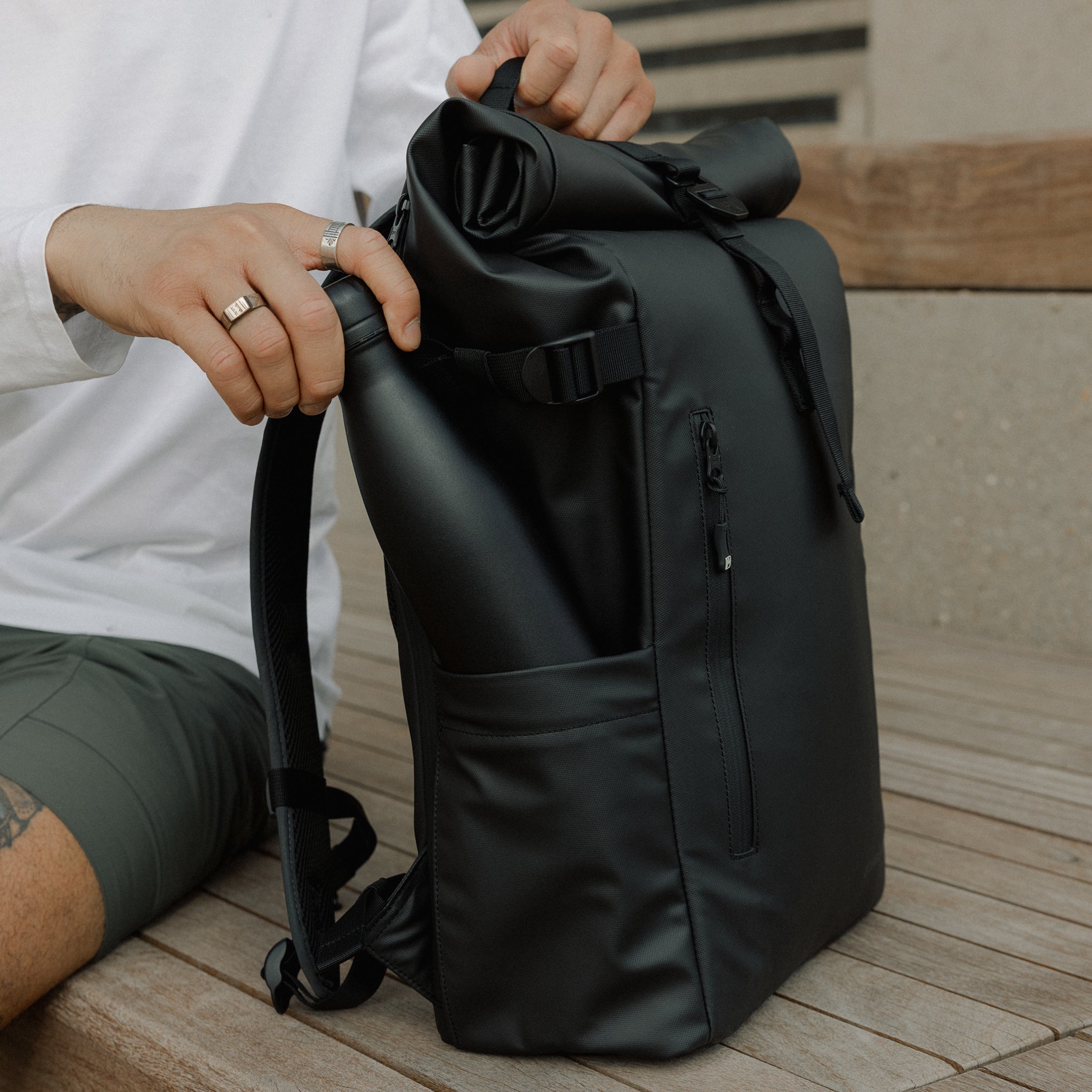 A man placing a bottle in the side bottle pocket on an All Black Roll Top 20L