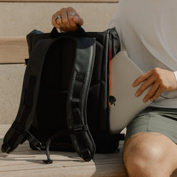 A close up of a man putting a laptop into an All Black Roll Top 20l