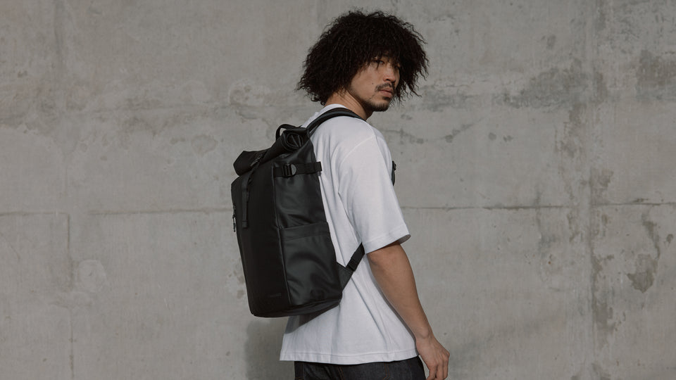 a lifstyle shot of a man facing away but looking at the camera wearing a hybrid backpack 30L on his back