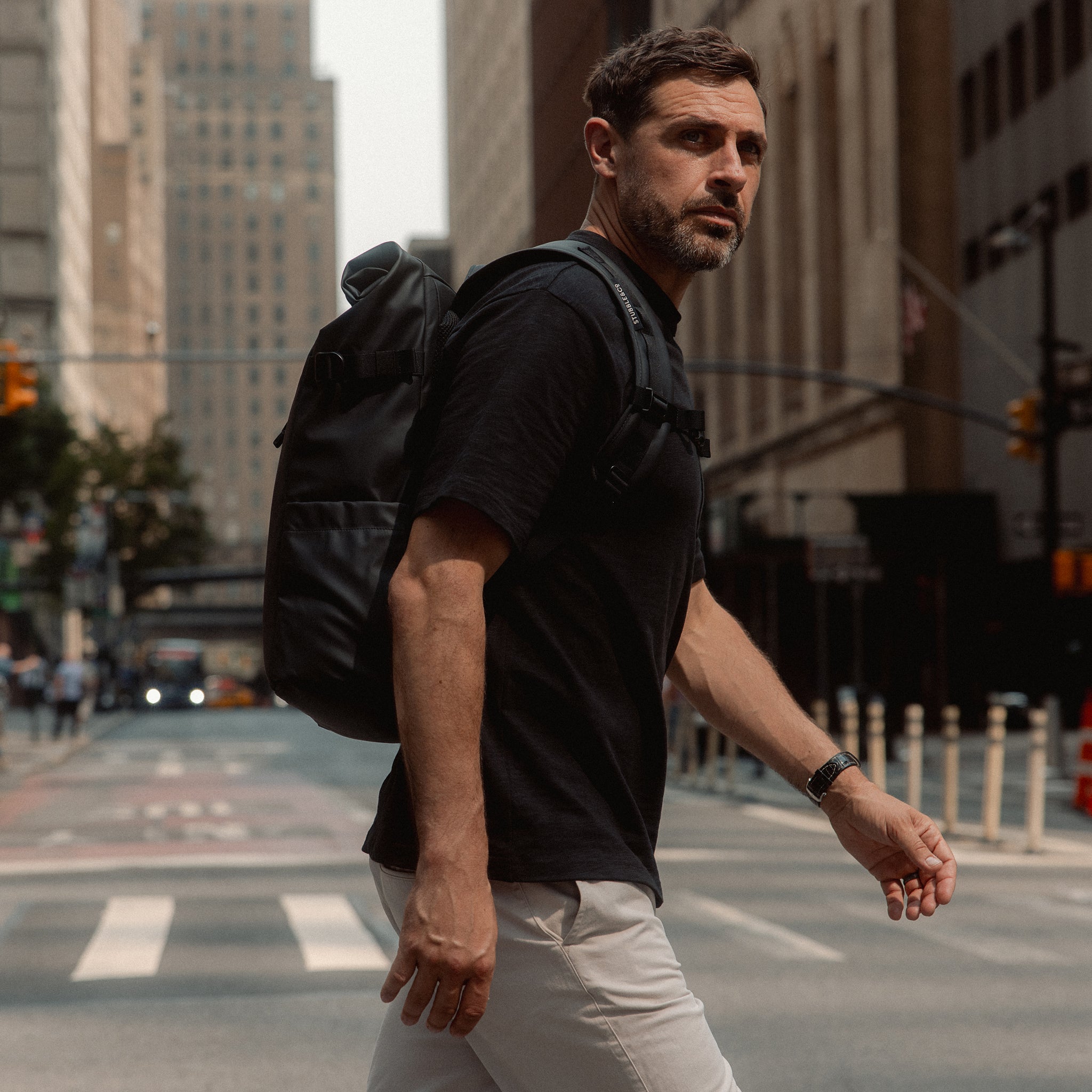 A man crossing the street in New York wearing an All Black Roll Top 20l on his back