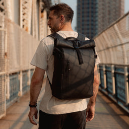 A man wearing an All Black Roll Top 20l on his back as he walks across a bridge