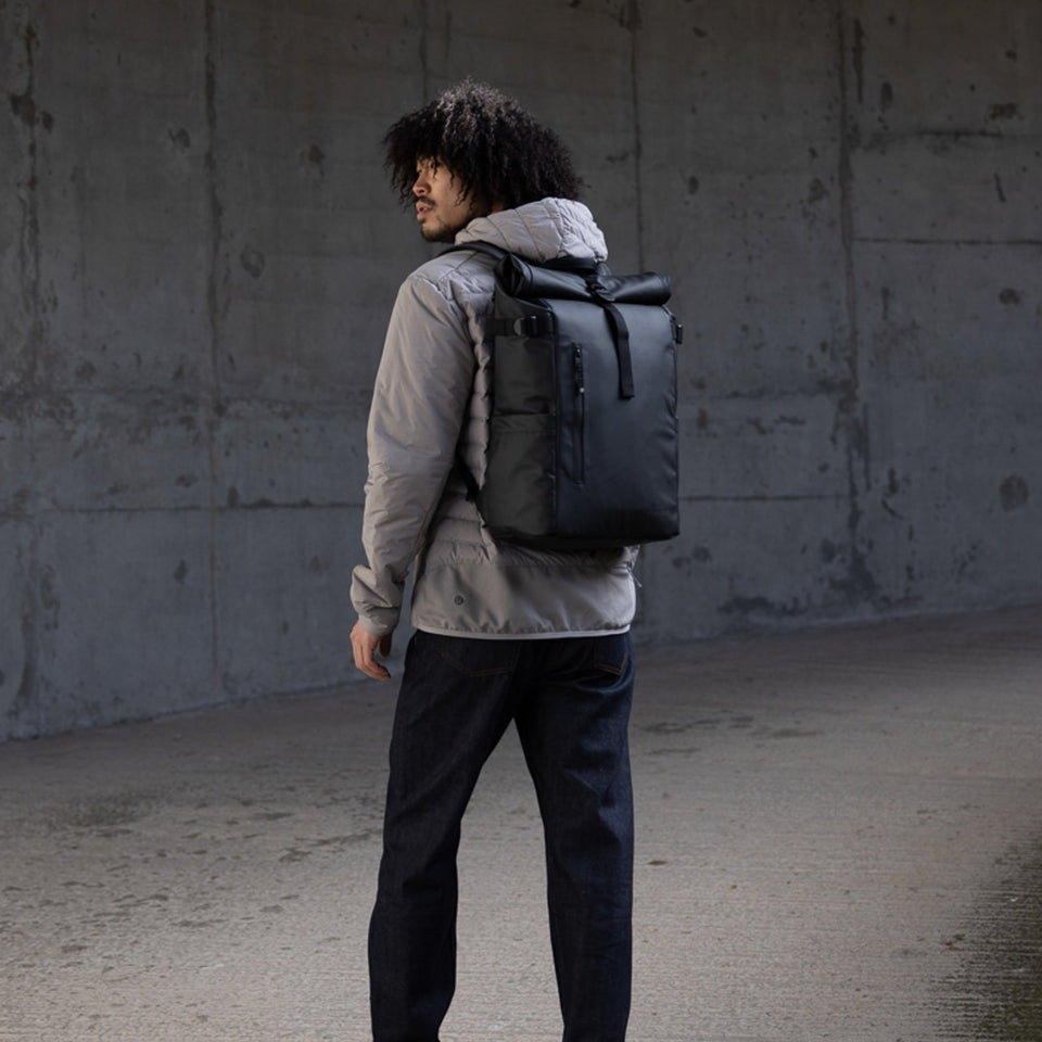 Roll Top black backpack on a person standing facing away