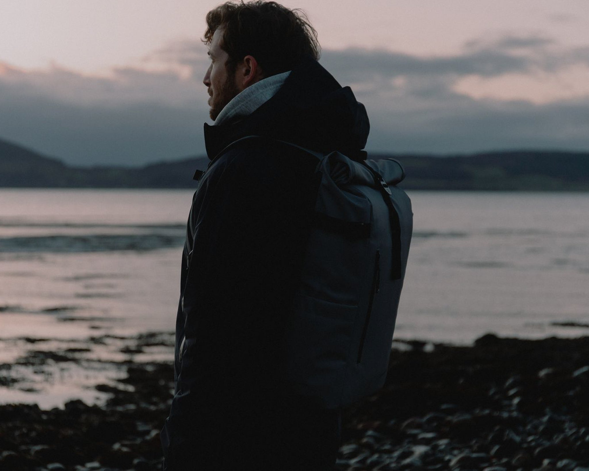 A man with a backpack on his back standing and looking out at a view of a lake. 