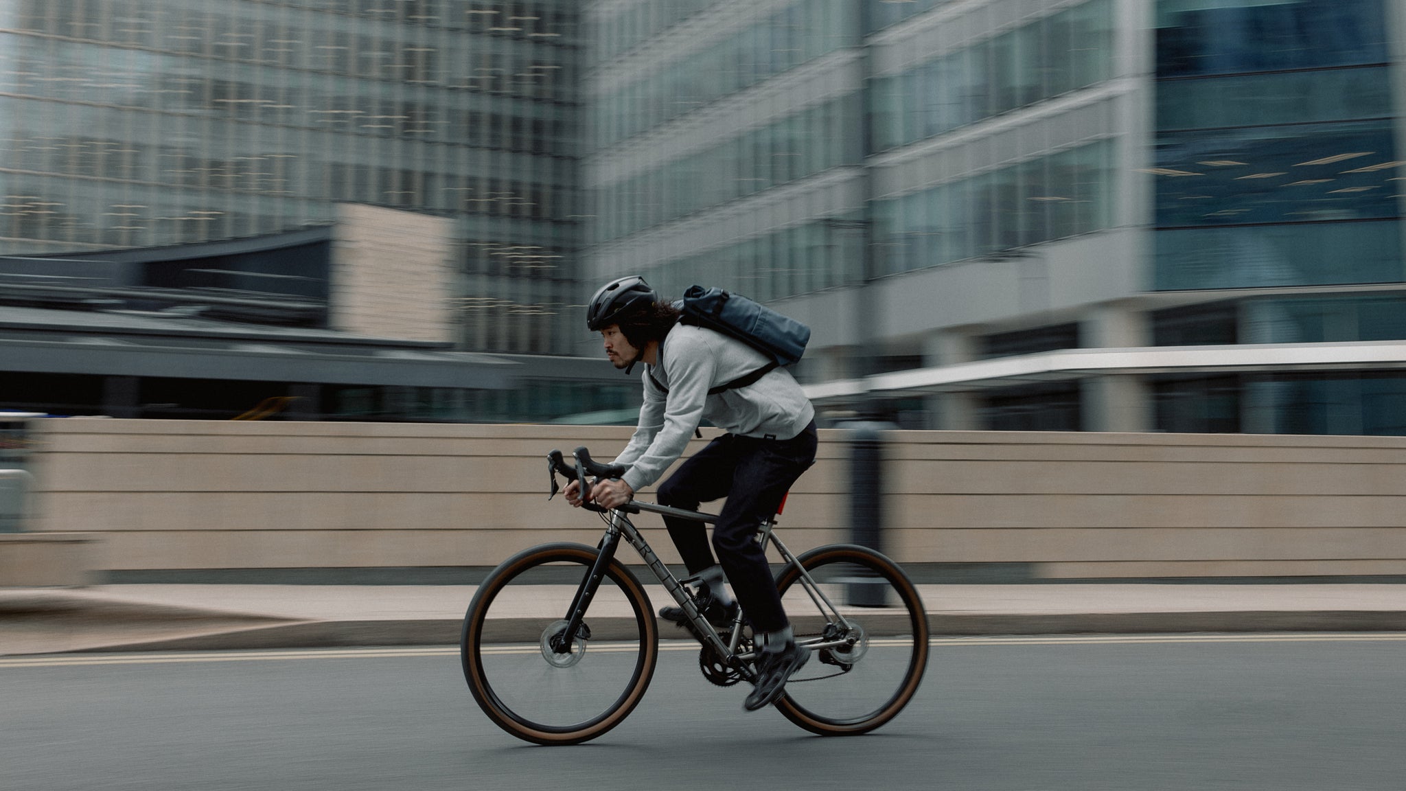 A photo of a man cycling past the camera with a tasmin blue roll top 20l on his back