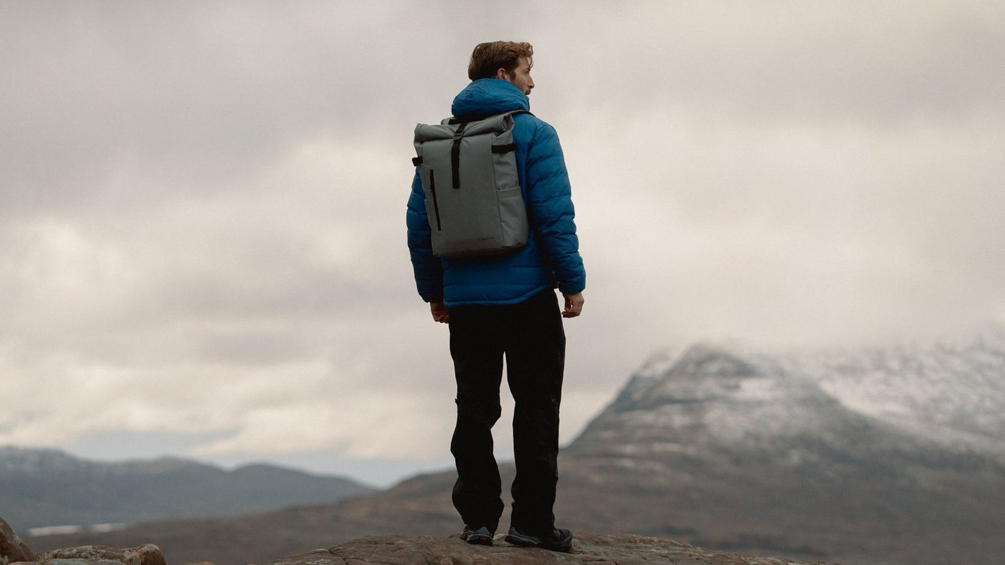 A man on top of a mountain has a backpack on and is admiring the view. 