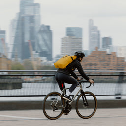 a woman cycling through the city with a Yellow roll top 20l on her back