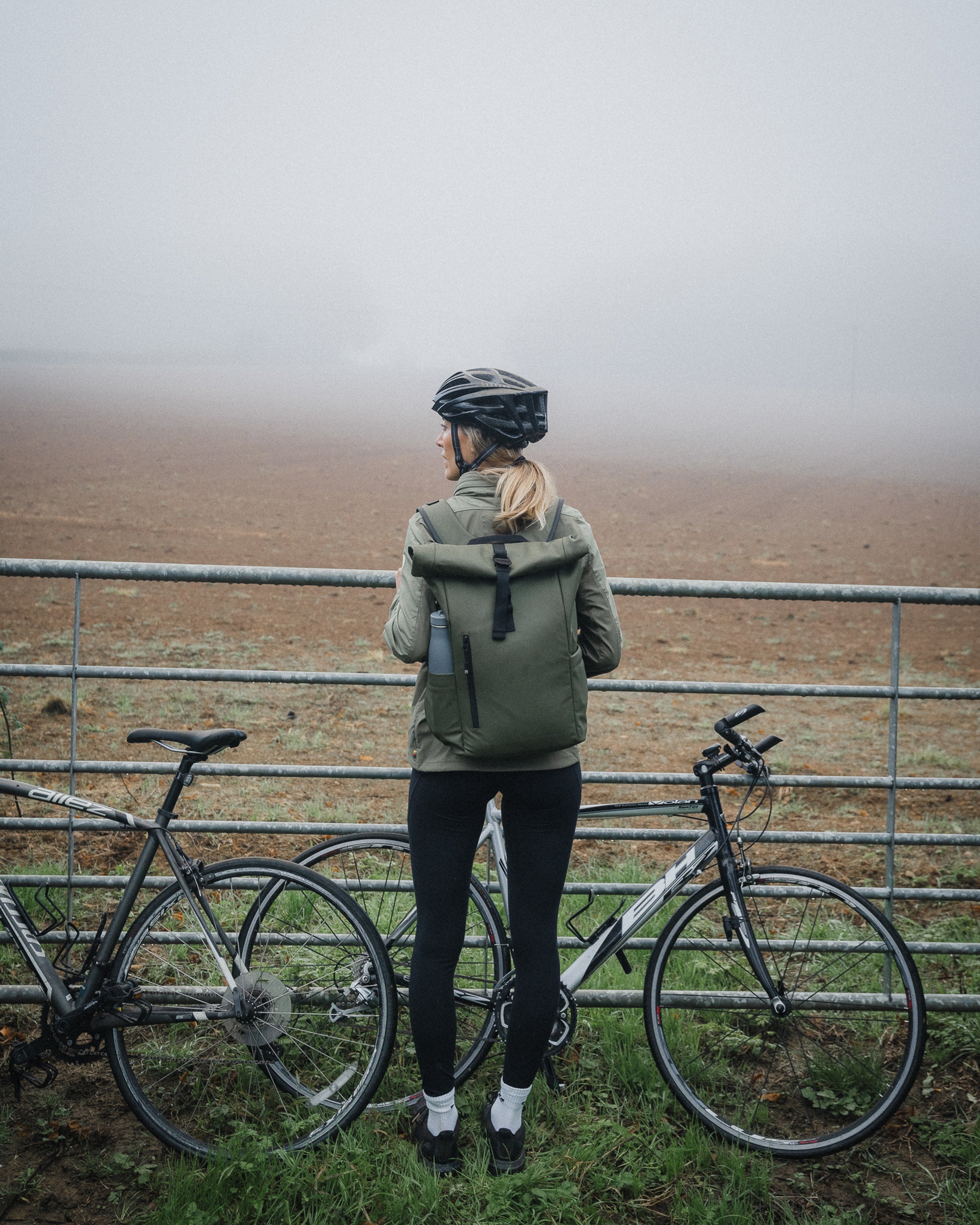 a woman standing by her bike with a roll top 15l in urban green on her back - the travel project blog