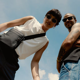 A man and woman looking down into the camera wearing an All Black shoulder bag