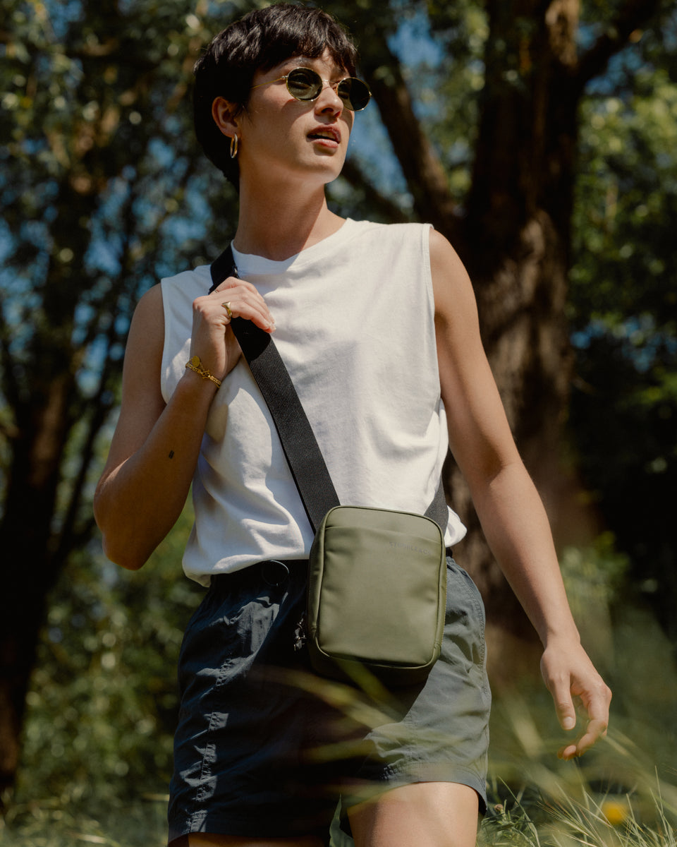 A woman walking through a field wearing an urban green shoulder bag