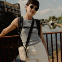 a woman standing on a bridge wearing a roll top and Sand shoulder bag