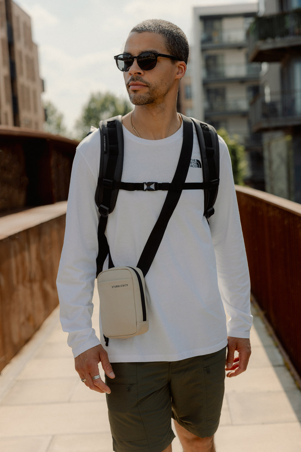 A male model wearing a roll top and sand shoulder bag