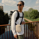 a man standing on a bridge wearing a roll top and Sand shoulder bag
