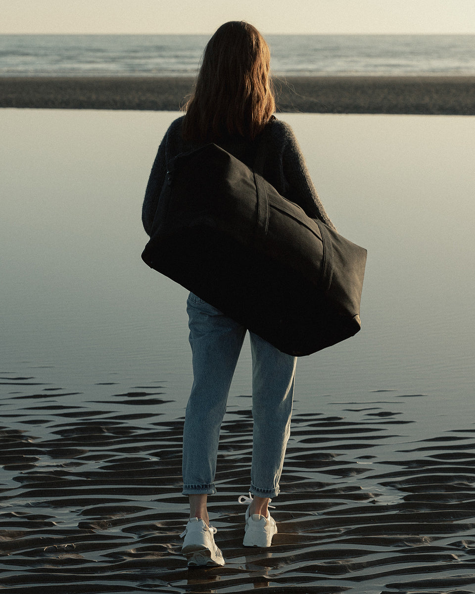 A woman wearing a Stubble and Co weekender duffel abg on her shoulder at the beach