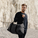 A man carrying the Weekender Outlet in Grey on his shoulder on a beach