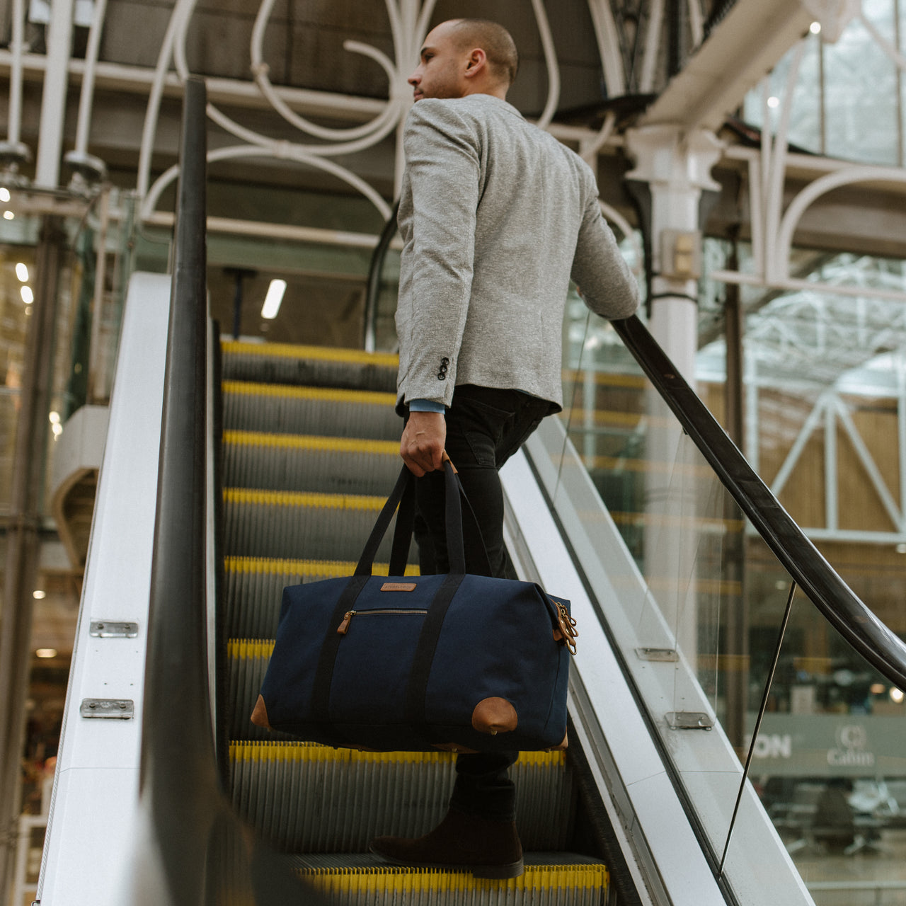 A man going up an esculator with a weekender outlet in his hand in Navy