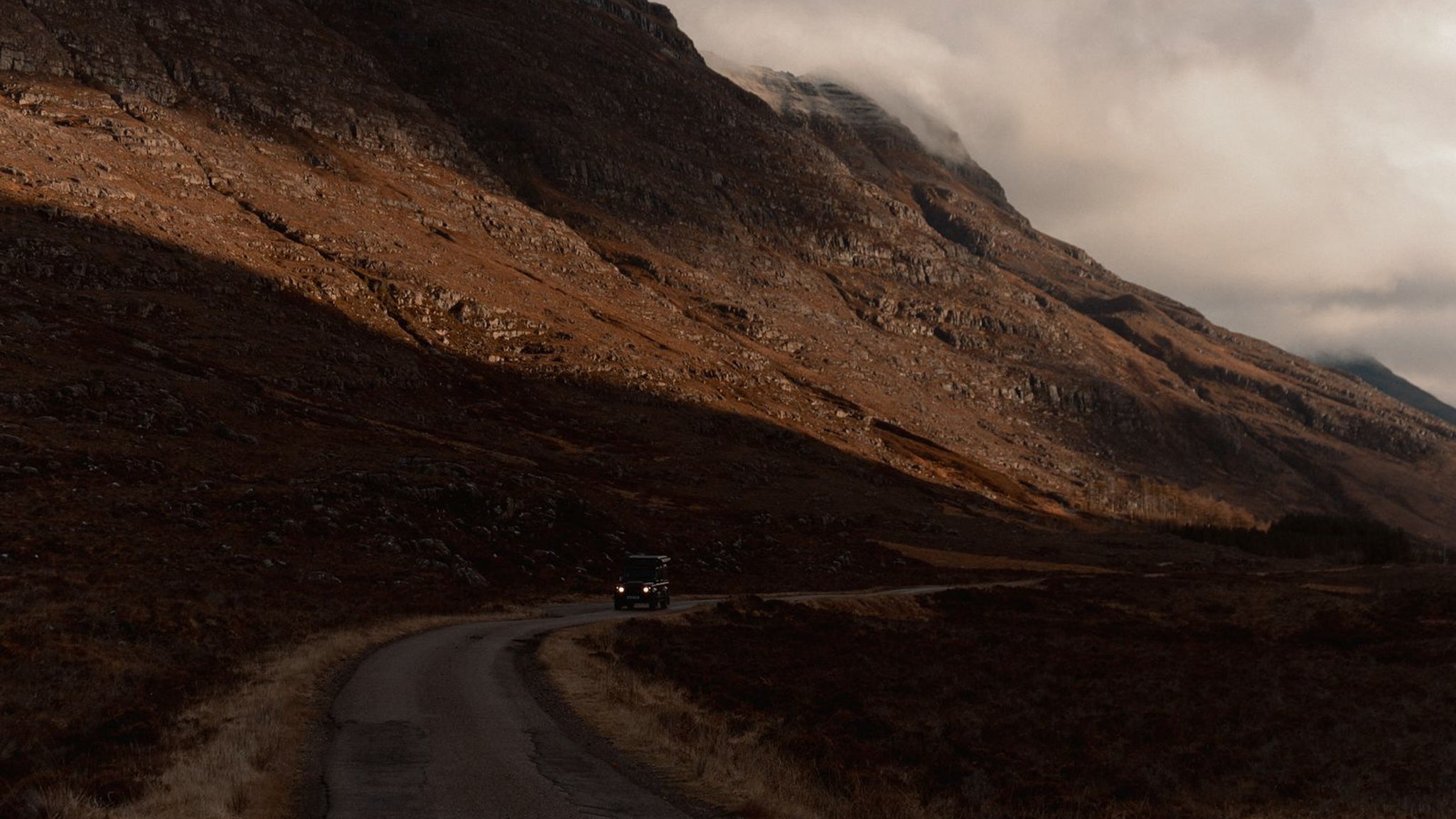 A Land Rover driving around a bend in the Scottish Highlands. 