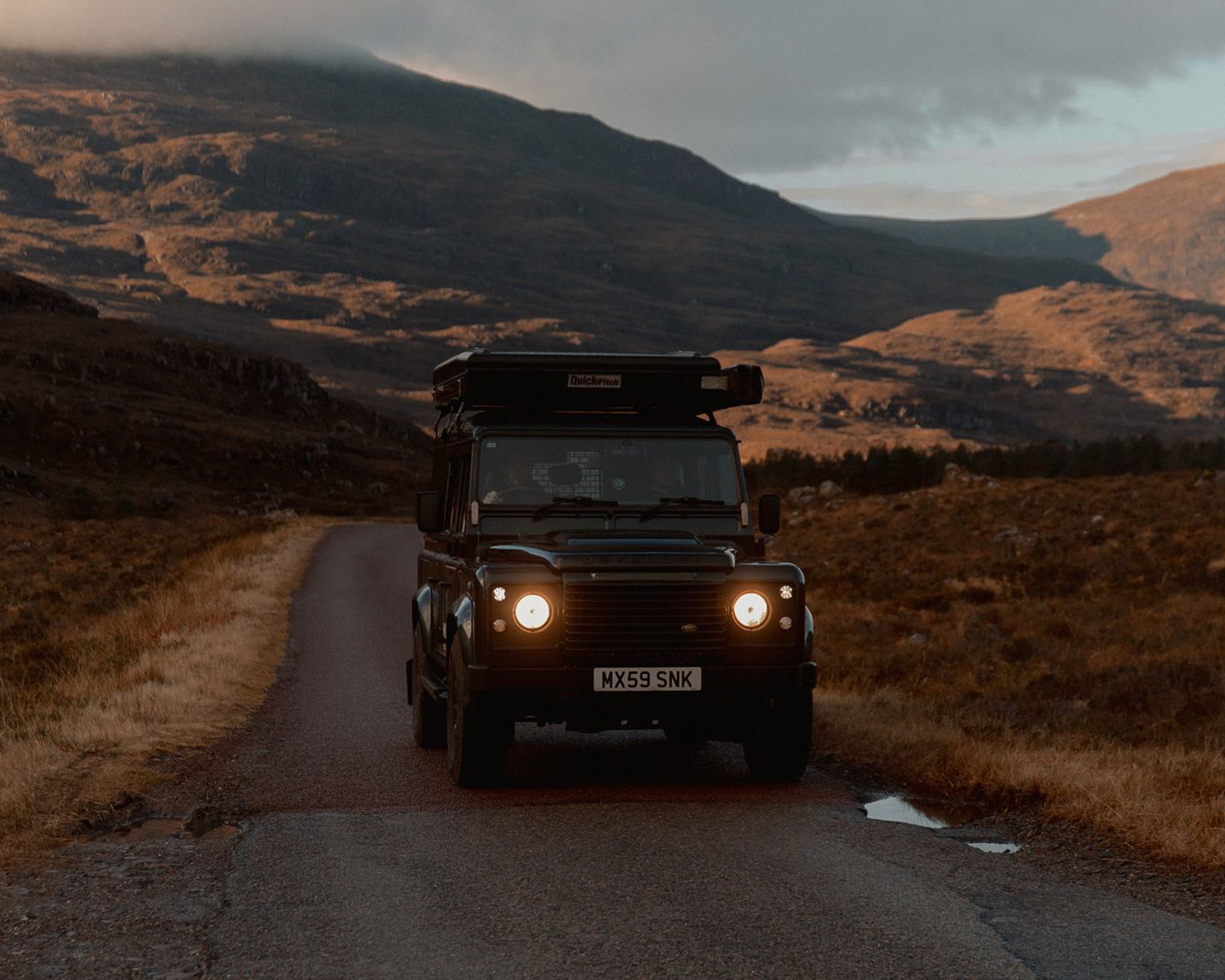 A land rover driving down a country road in the Scottish Highlands. 