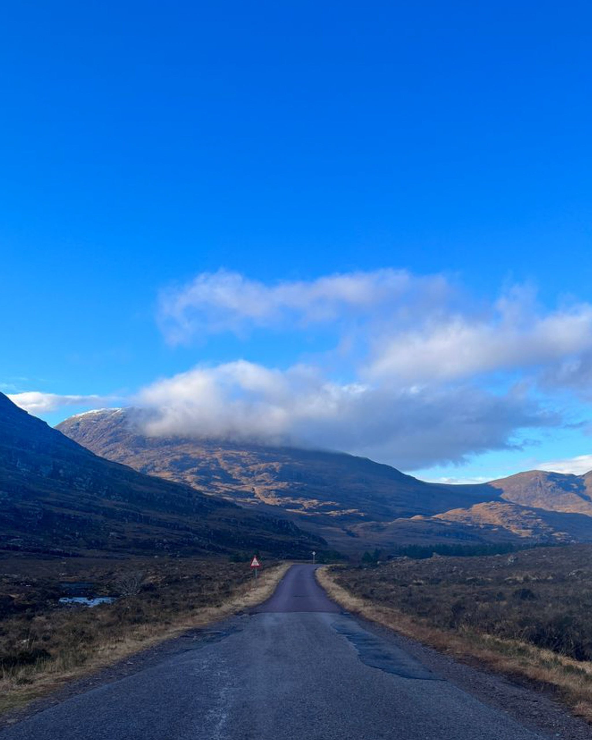 A view of a road with mountains and a blue sky in the Scottish Highlands. 